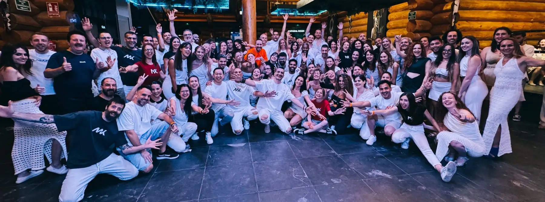 Around ninety dancers dressed in white, many in MetaKizz T-shirts, posing together and reaching towards the camera